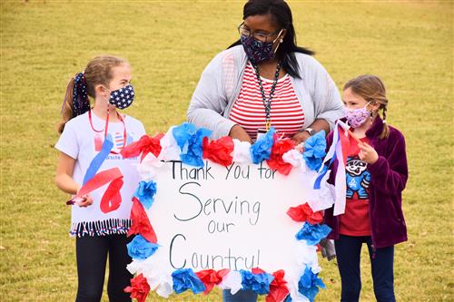 Teacher with two students holding sign thanking veterans for serving our country 